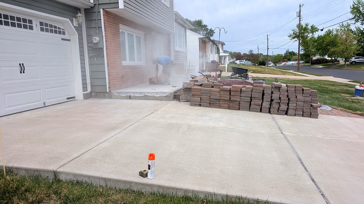 Crew member cutting pavers to size next to a stacked pallet of pavers