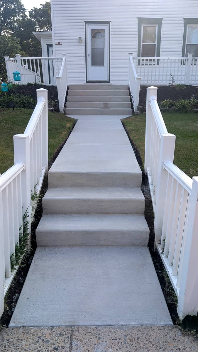 After: brand-new poured concrete steps and walkway between white railings with fresh planting beds