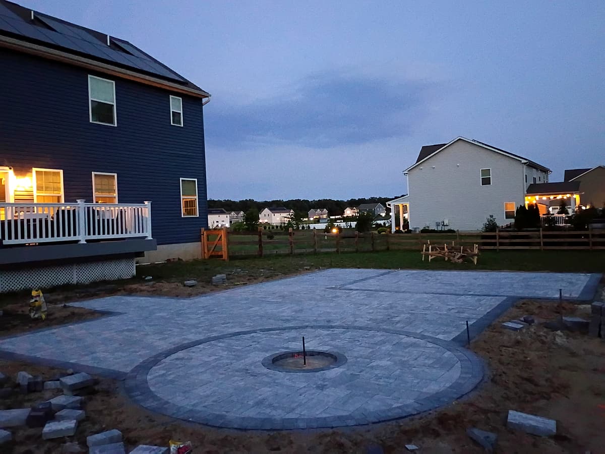 Custom paver fire pit and circular surround taking shape at dusk in a South Jersey backyard