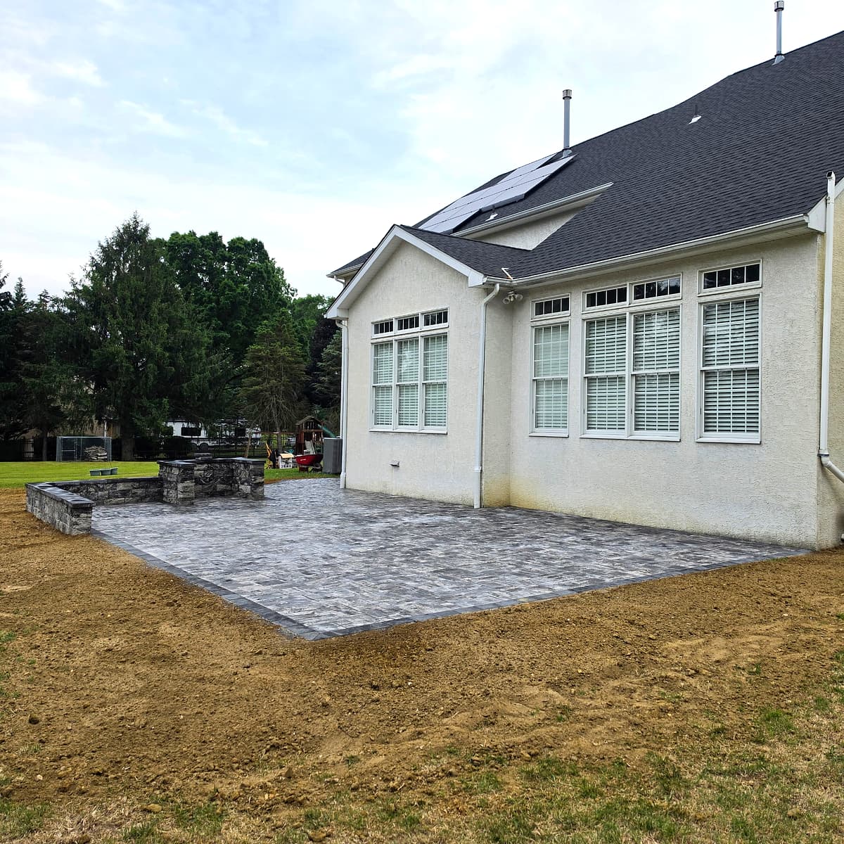 Paver patio with built-in outdoor stone fireplace behind a South Jersey home