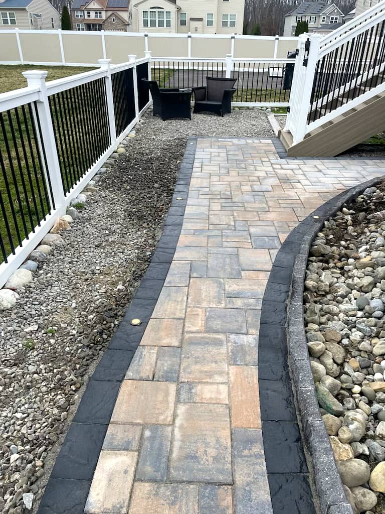 Paver walkway with pebble border beside a white deck railing