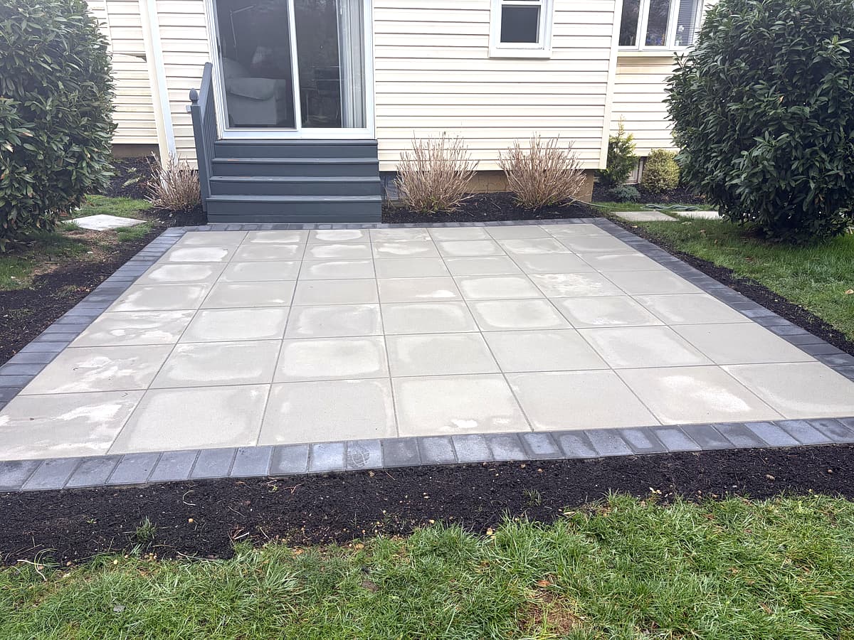 Slab-style paver patio with charcoal border and fresh mulch beds