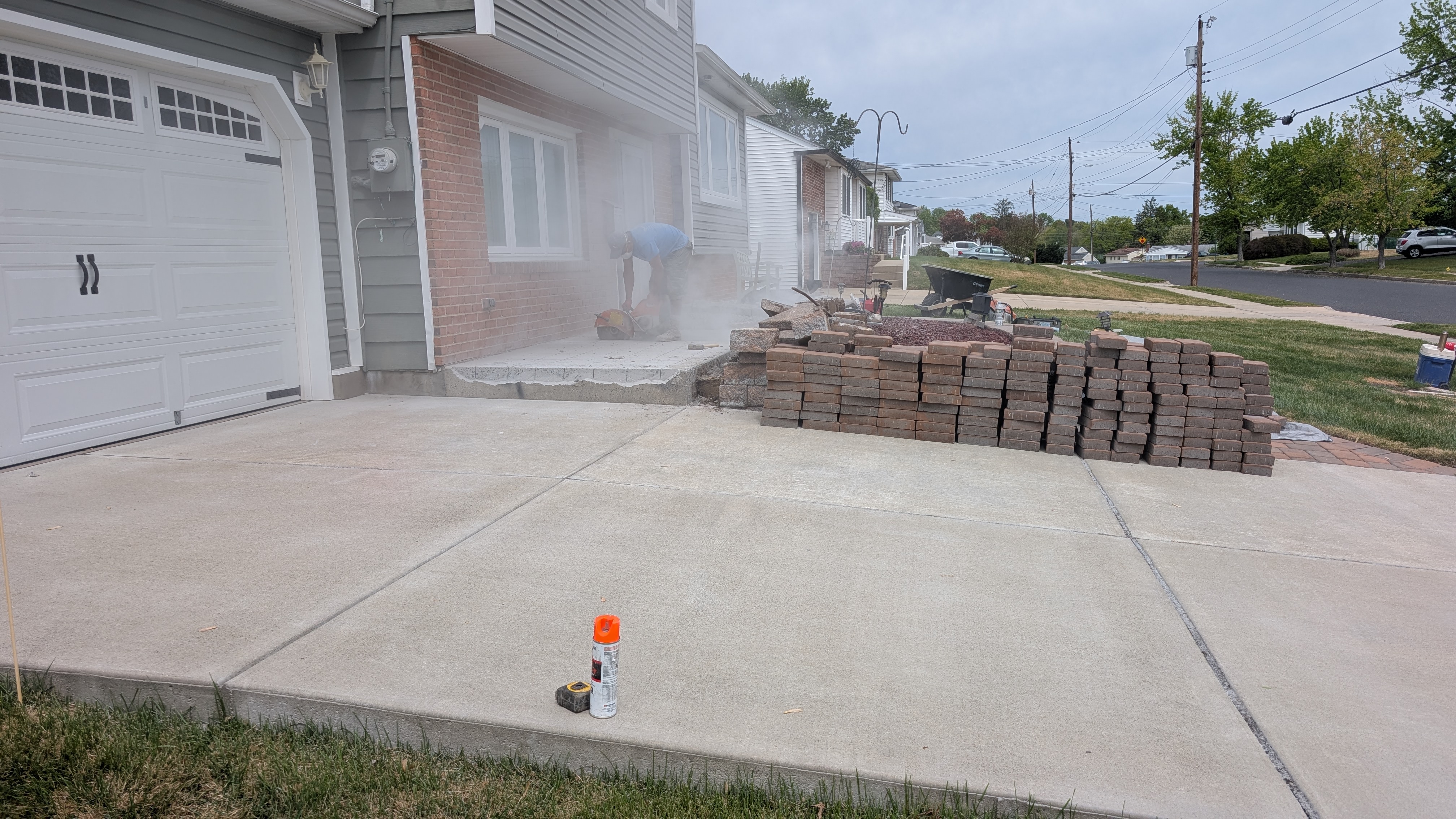 Crew member cutting pavers to size next to a stacked pallet of pavers