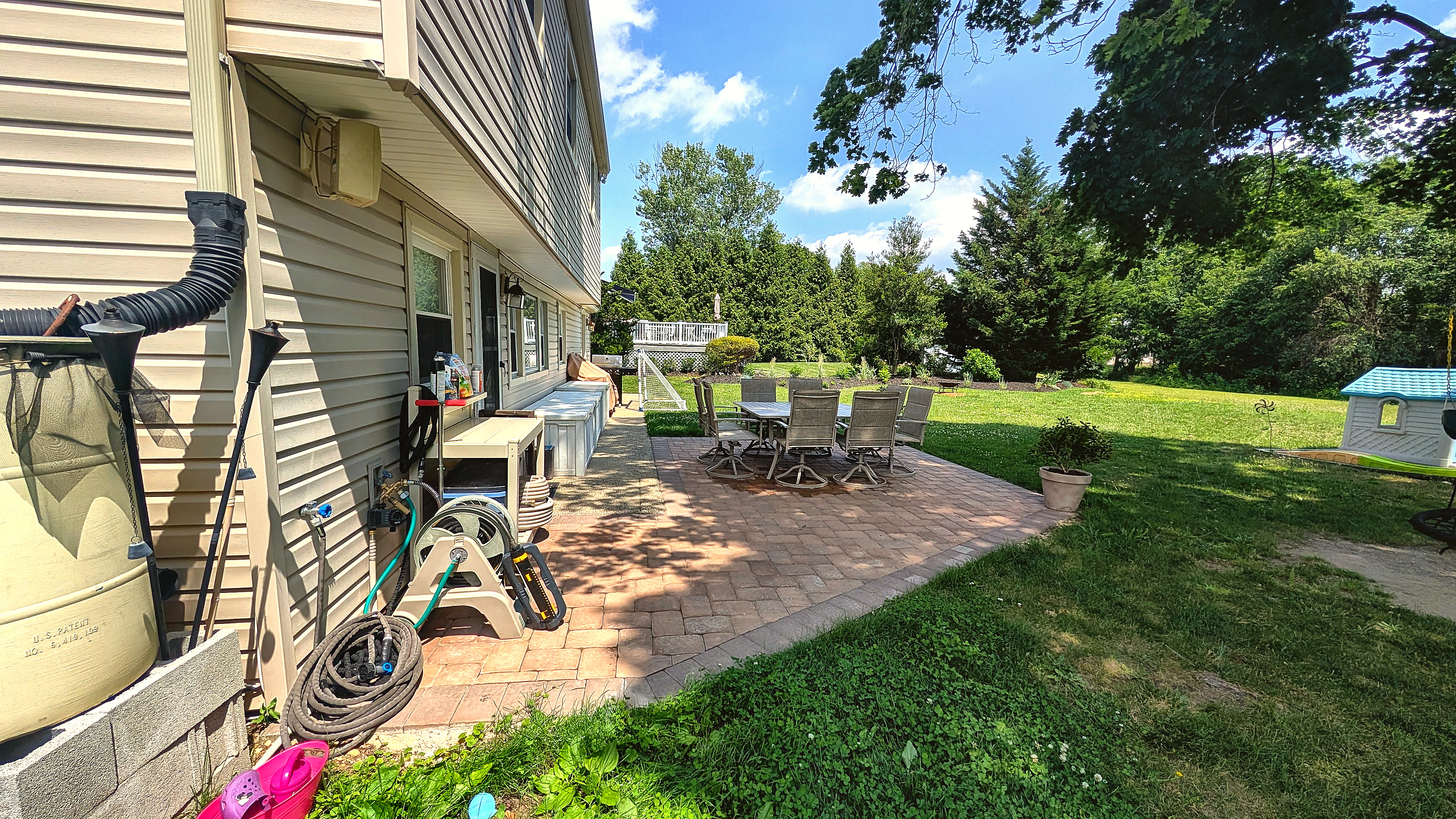 Large backyard paver patio bordered by lawn and mature trees